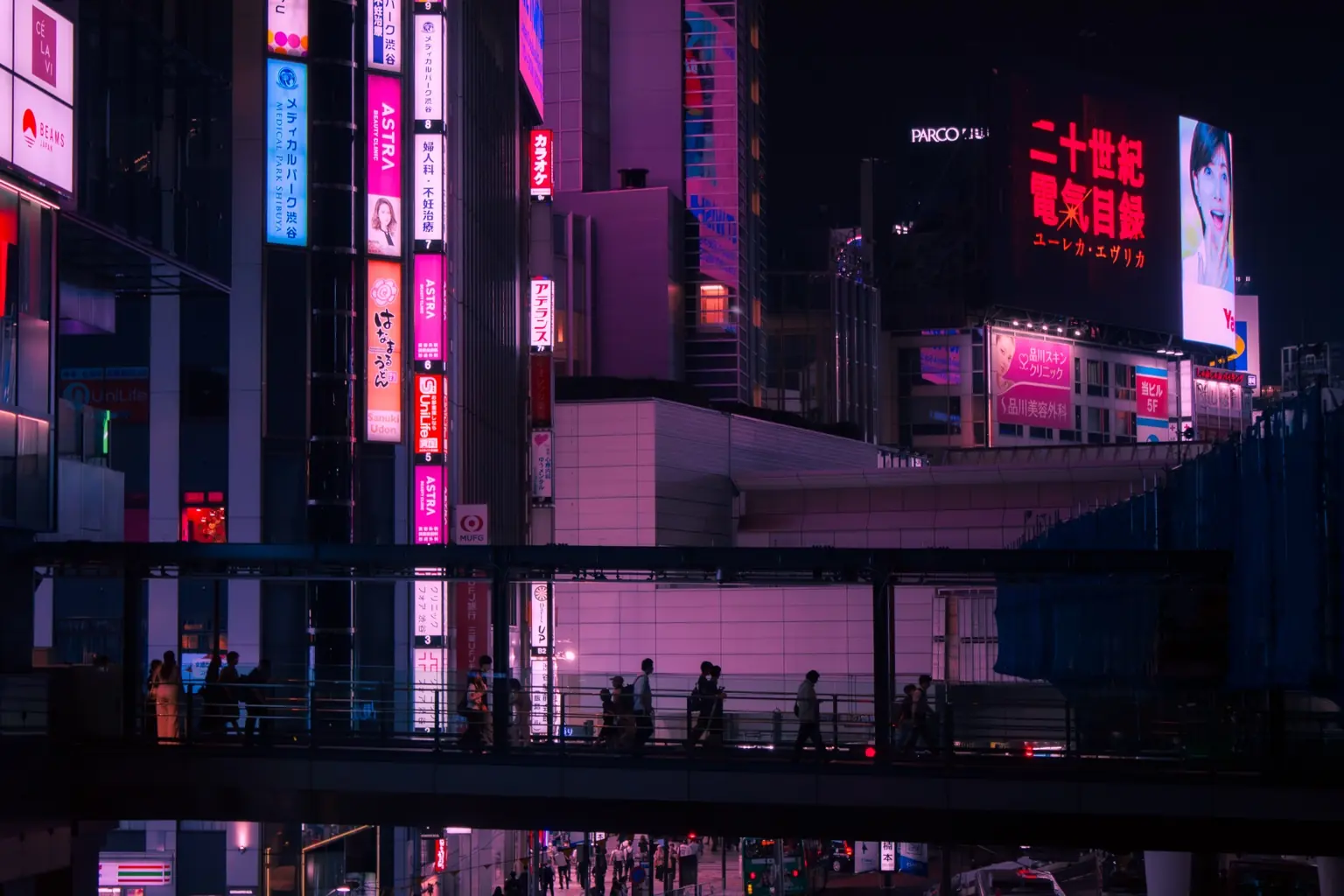 Pedestrians crossing an elevated walkway beneath vivid signs in Tokyo at night