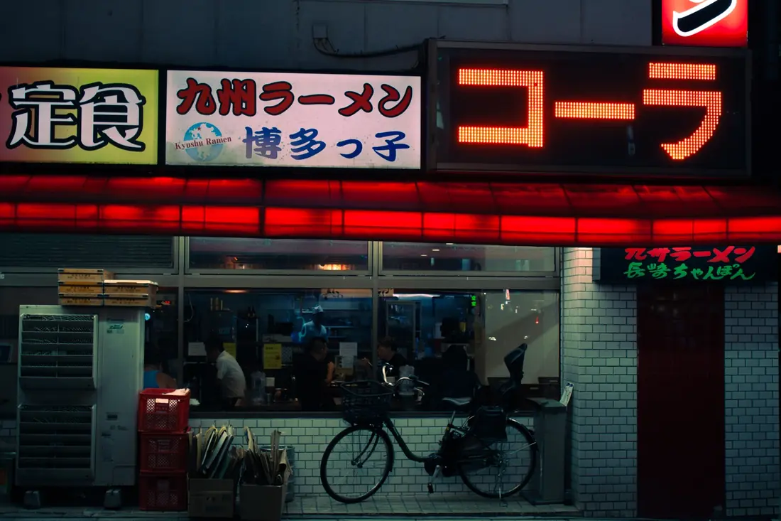 A bicycle parked outside a red-lit ramen shop at night