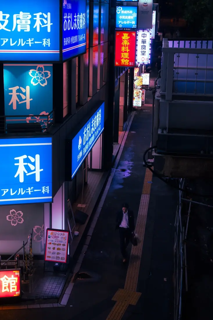 A lone pedestrian in a narrow alley beneath luminous Japanese signs