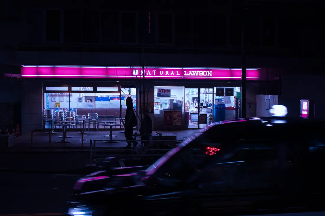 A moving taxi reflecting the magenta light of a convenience store