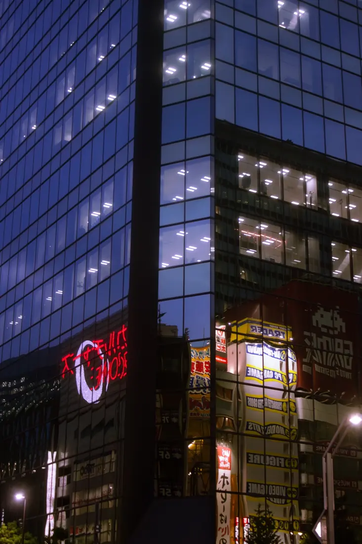Tokyo signs reflected across blue glass office buildings at dusk