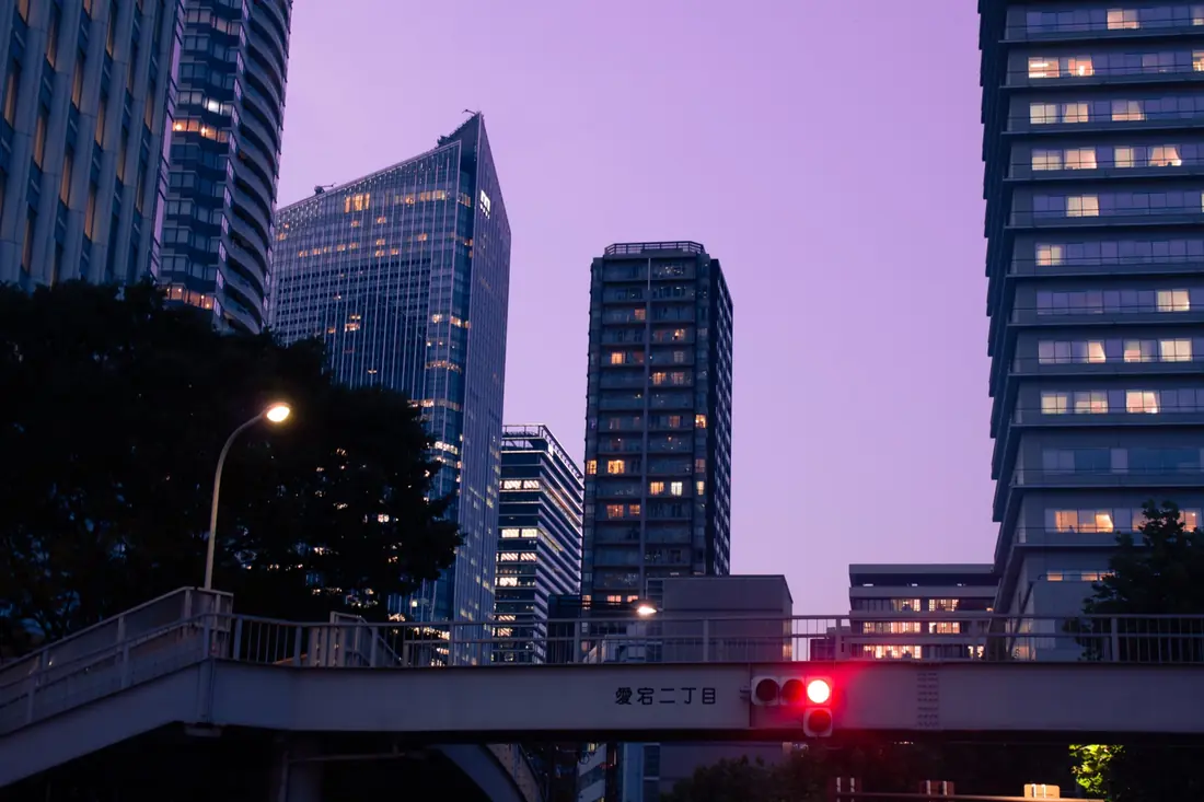 A violet dusk skyline divided by a pedestrian bridge and red traffic light