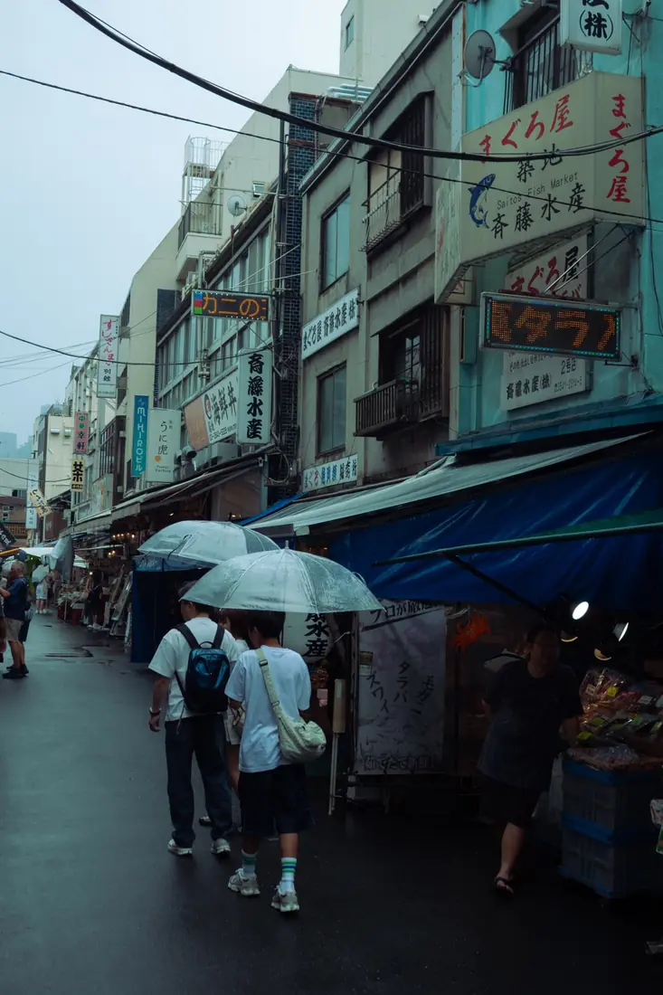 Shoppers walking beneath clear umbrellas through a rainy fish market