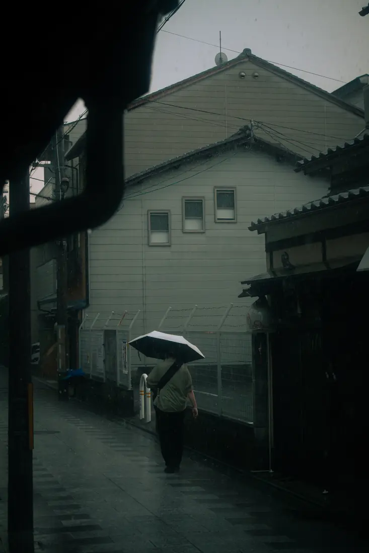 A lone figure carrying an umbrella down a dark rain-soaked lane