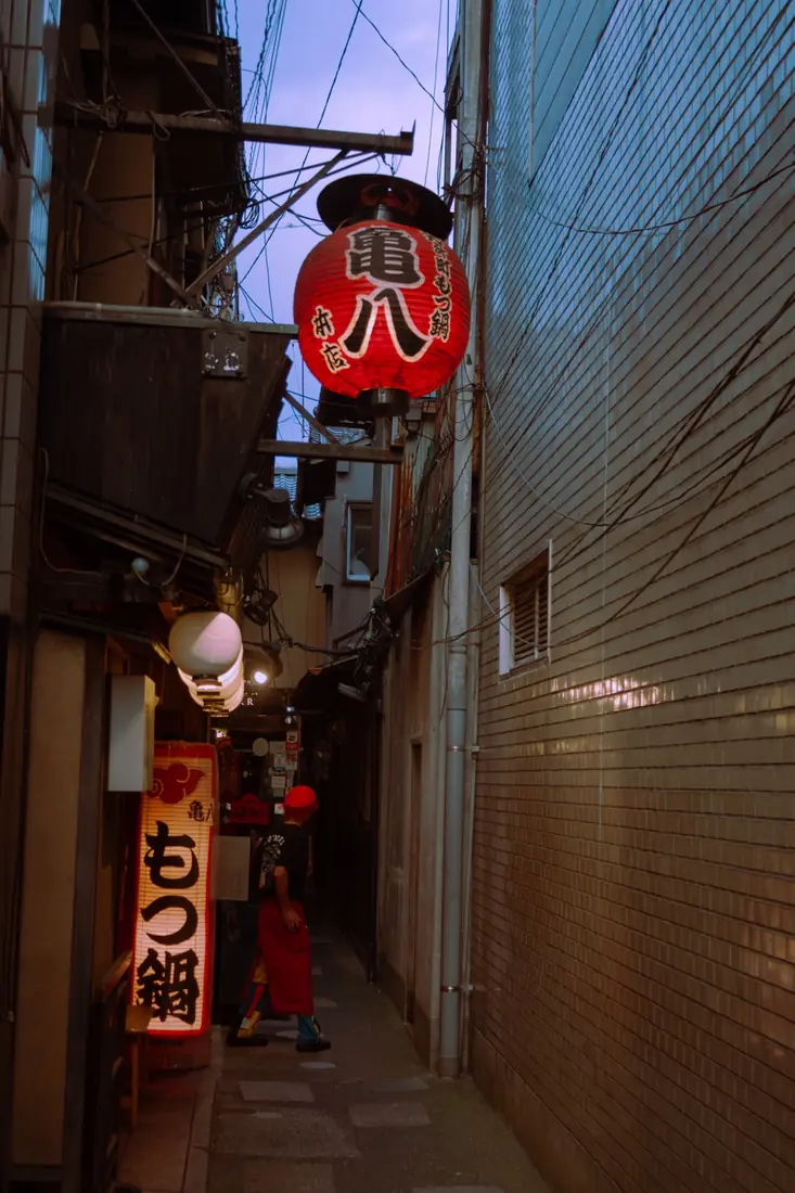 A restaurant worker beneath a red lantern in a narrow Kyoto alley