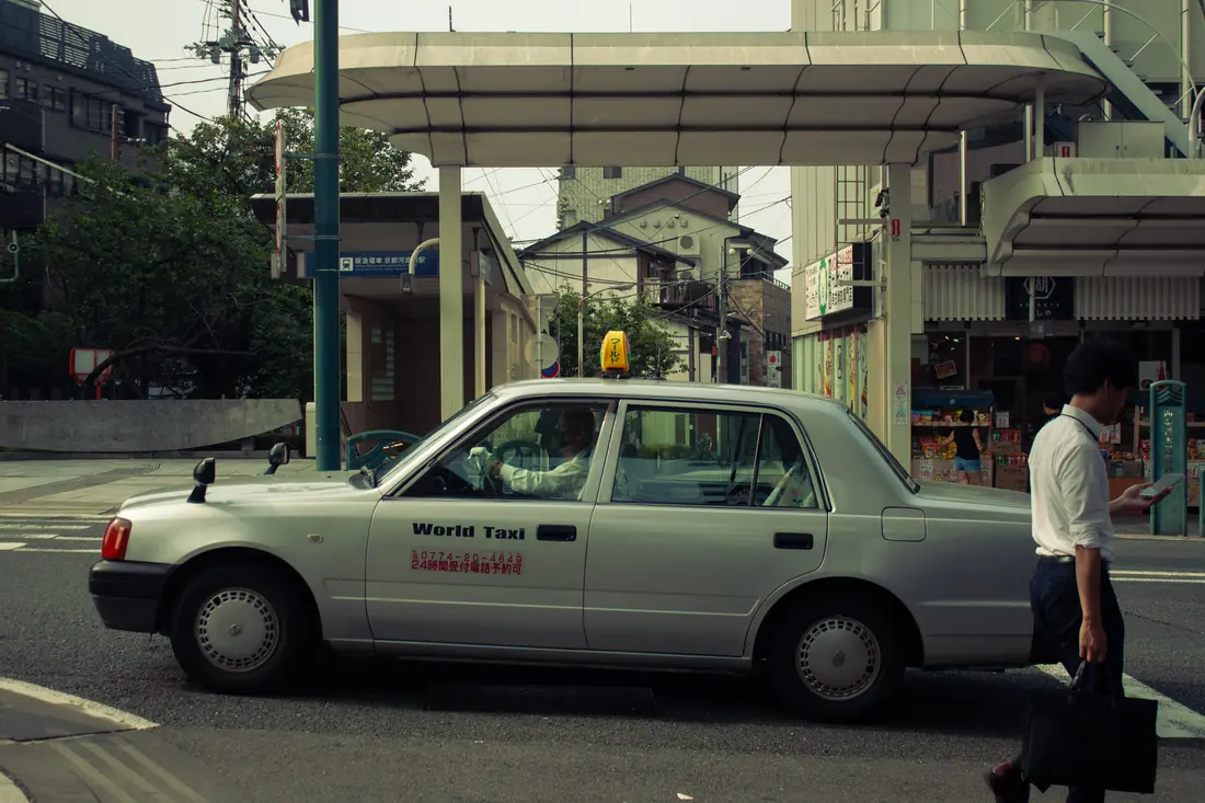 A white taxi passing a pedestrian on a quiet Kyoto street